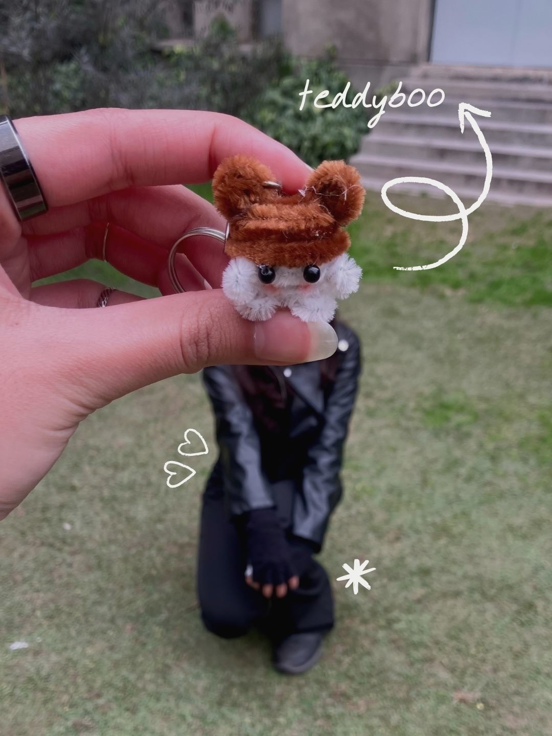 Small plush keychain held by a hand with decorative text overlay on a grassy background