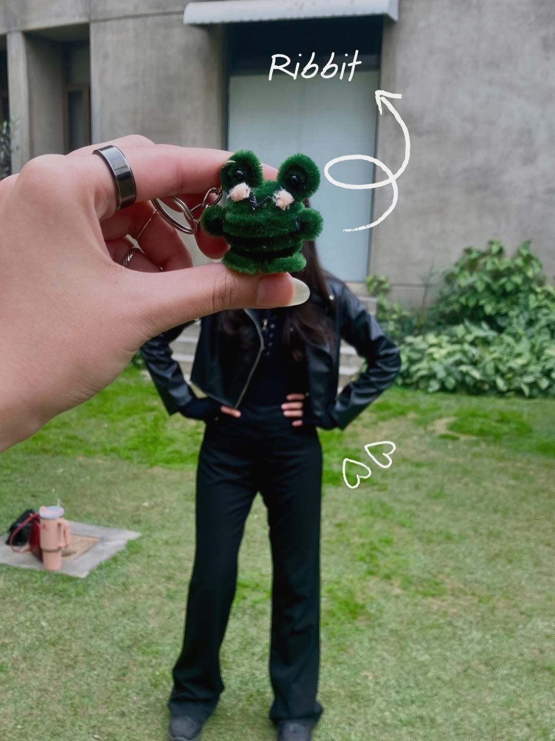 Hand holding a green frog-shaped keychain with a person in the background