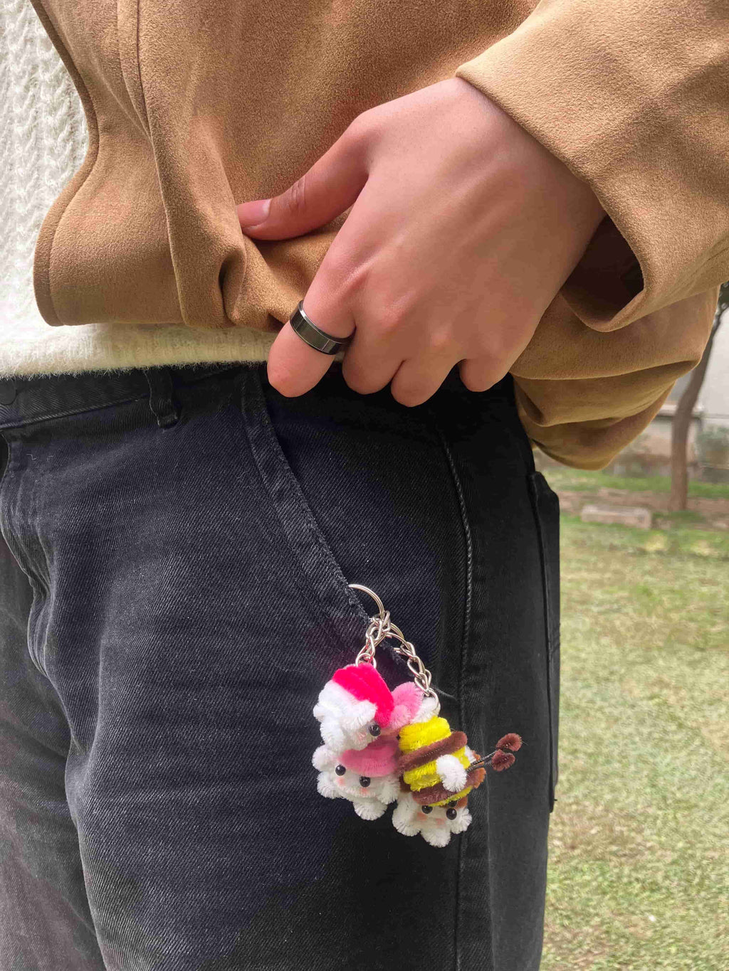 Person wearing a colorful keychain with fluffy attachments on dark jeans outdoors.