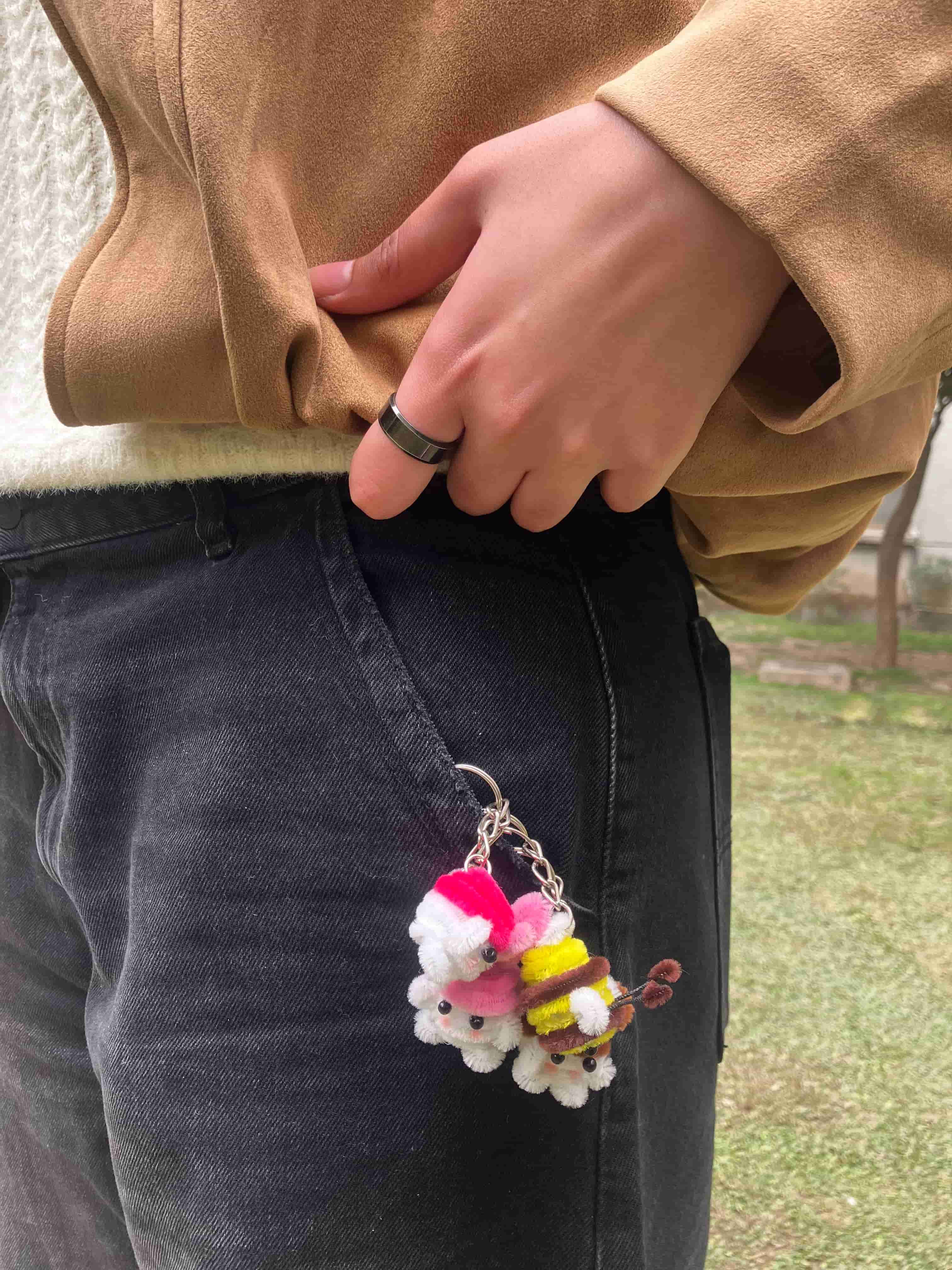 Person wearing a colorful keychain with fluffy attachments on dark jeans outdoors.