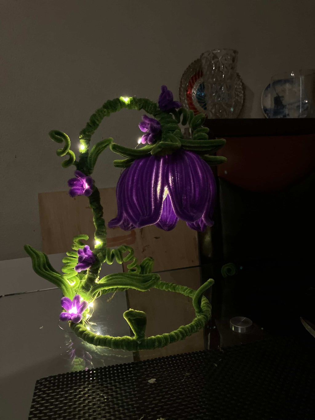 Decorative string light shaped like a flower with purple flowers and green stems on a plain background.