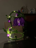 Decorative string light shaped like a flower with purple flowers and green stems on a plain background.