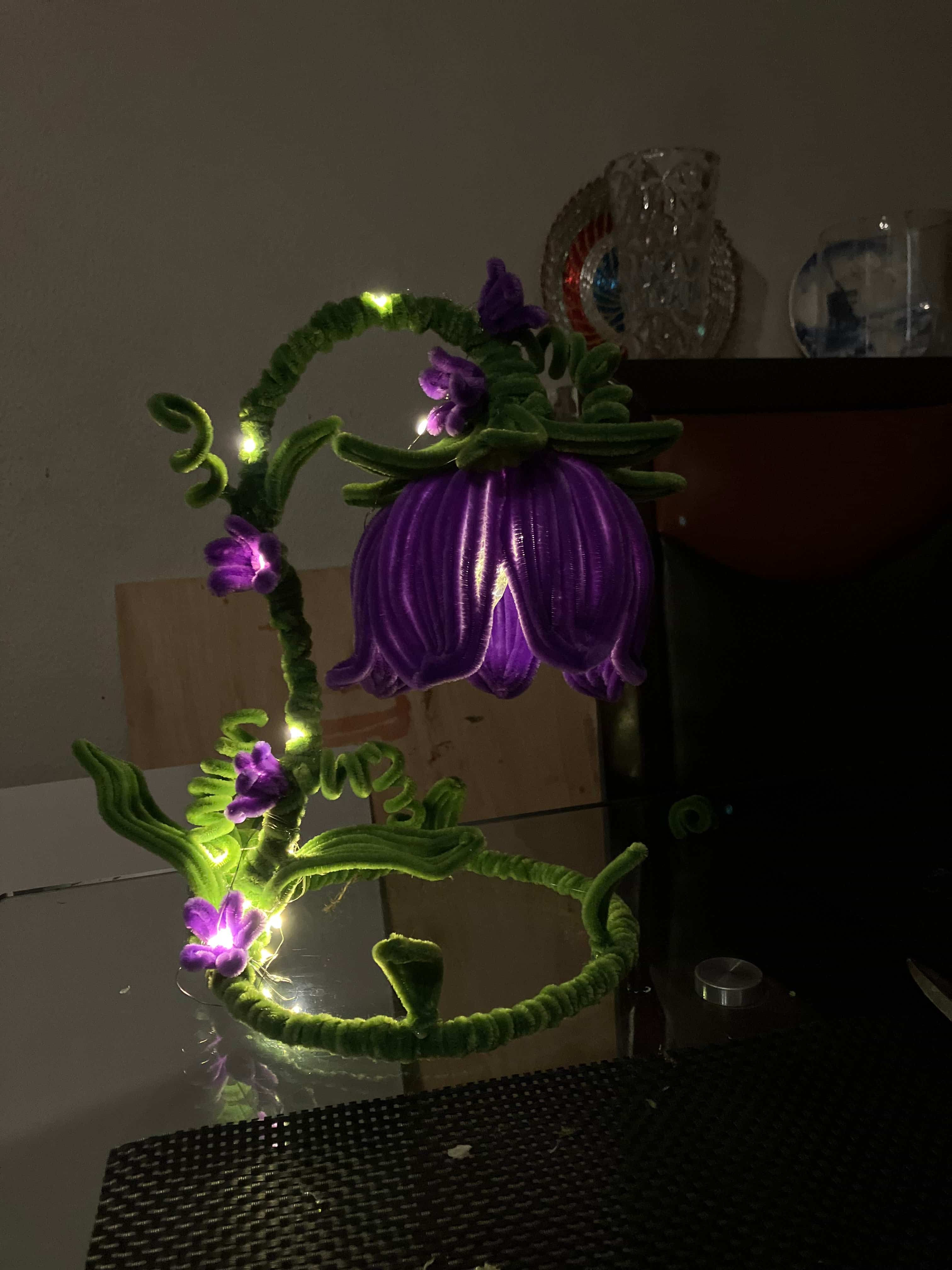Decorative string light shaped like a flower with purple flowers and green stems on a plain background.