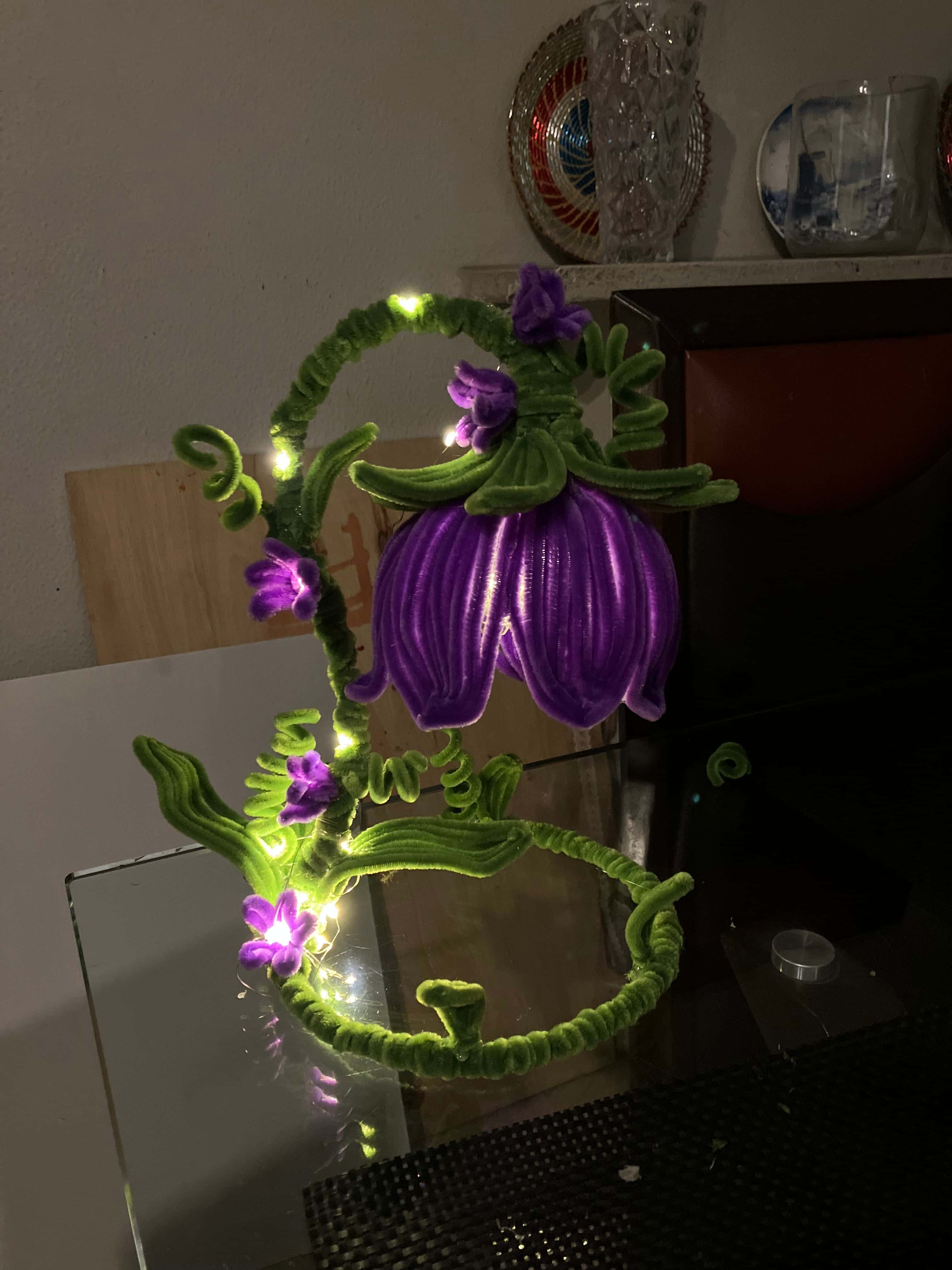 Decorative headband with purple flowers and green straps on a reflective surface.
