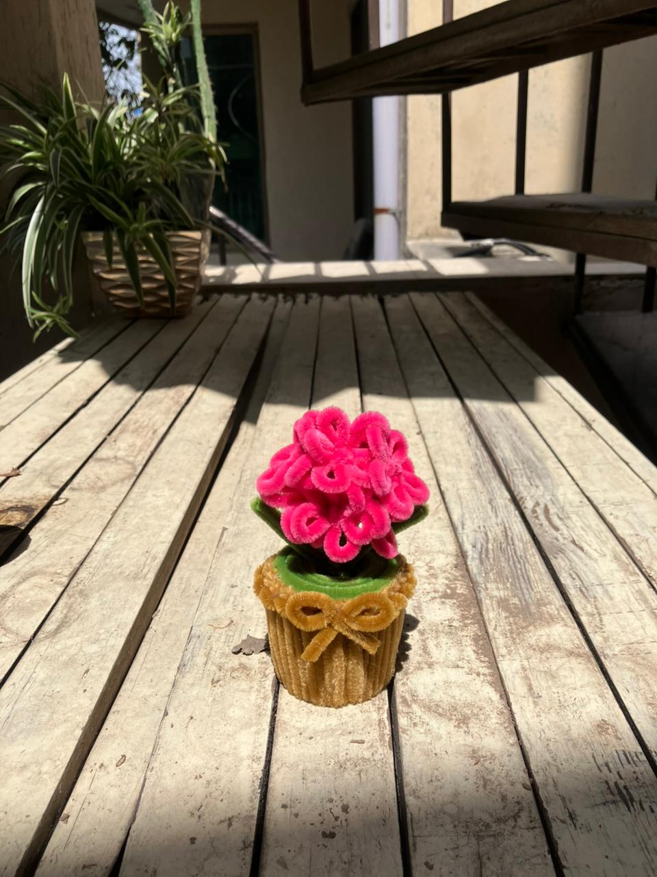 Pink knitted flower in a brown pot on a wooden deck