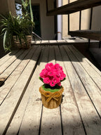 Pink knitted flower in a brown pot on a wooden deck