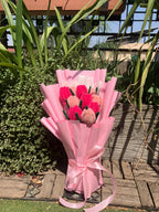 Bouquet of pink and red tulips wrapped in pink paper with a ribbon, set against a natural background.