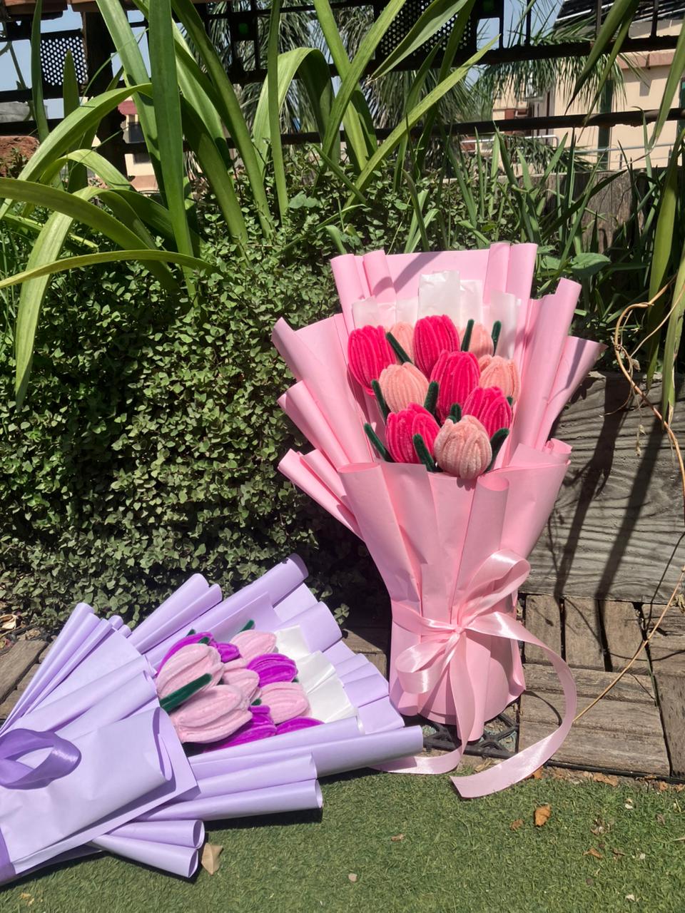 Bouquets of flowers wrapped in pink and purple paper with ribbons on a grassy area.