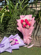 Bouquets of flowers wrapped in pink and purple paper with ribbons on a grassy area.