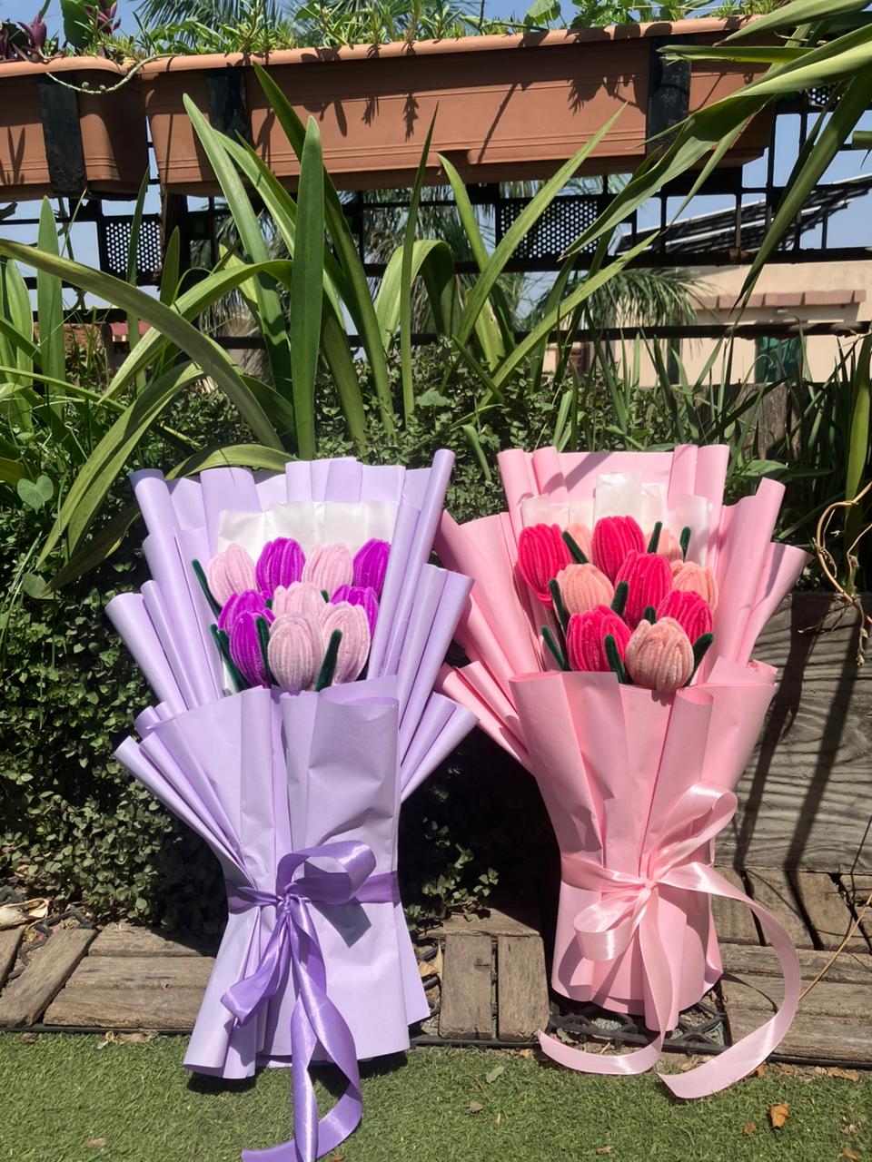 Two bouquets of artificial tulips wrapped in purple and pink ribbons on a grassy background.