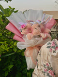 Bouquet of flowers wrapped in pink and white paper with a floral-patterned fabric in the background.