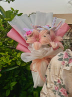 Bouquet of flowers wrapped in pink and white paper with a floral-patterned fabric in the background.