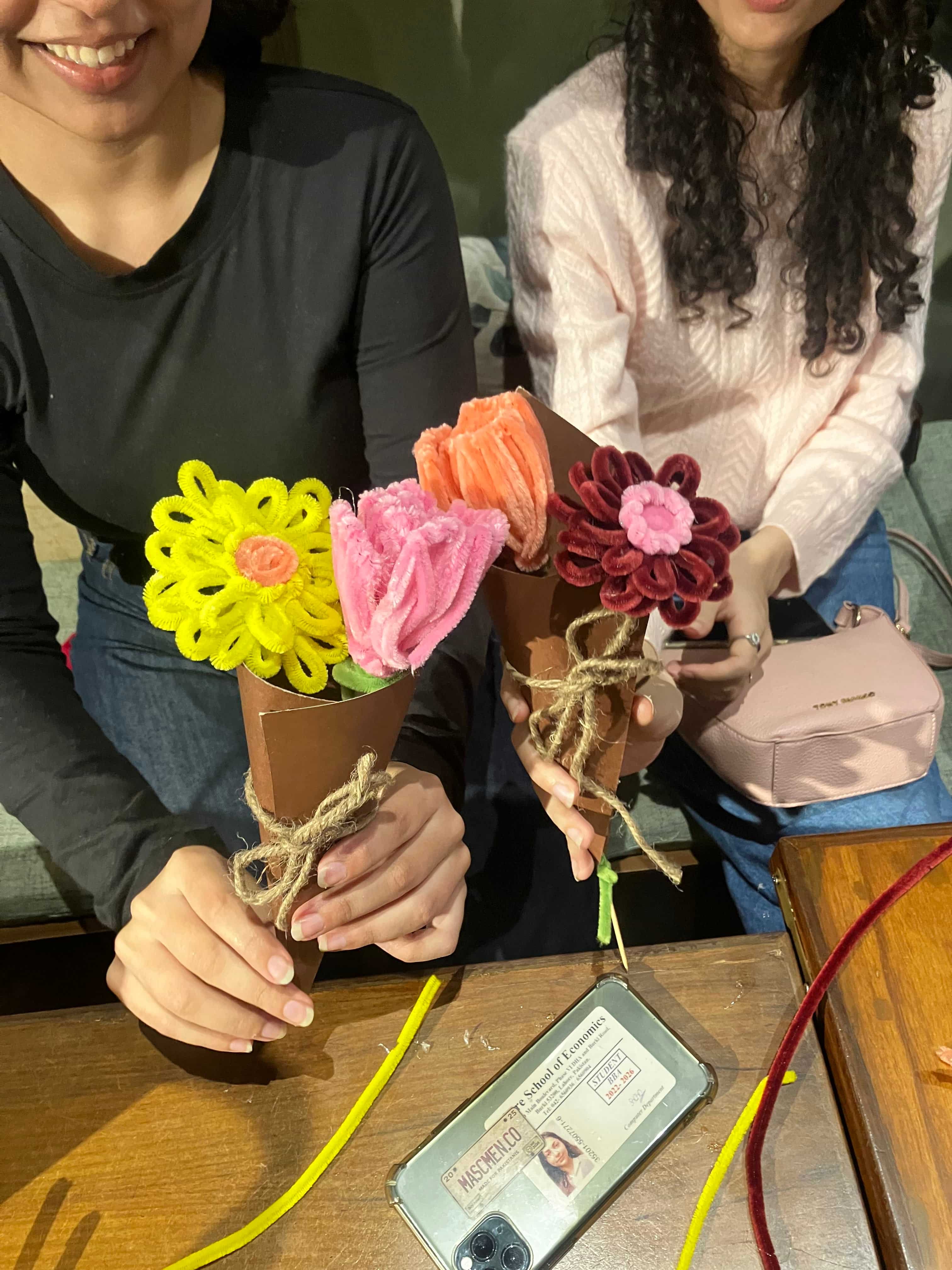 Person holding a bouquet of colorful flowers with a wooden table and ID card in the background.