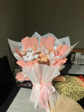 Bouquet of flowers wrapped in pink and white paper with a pink ribbon on a dark surface.