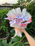 Decorative flower arrangement with ribbons held by a hand against a green outdoor background