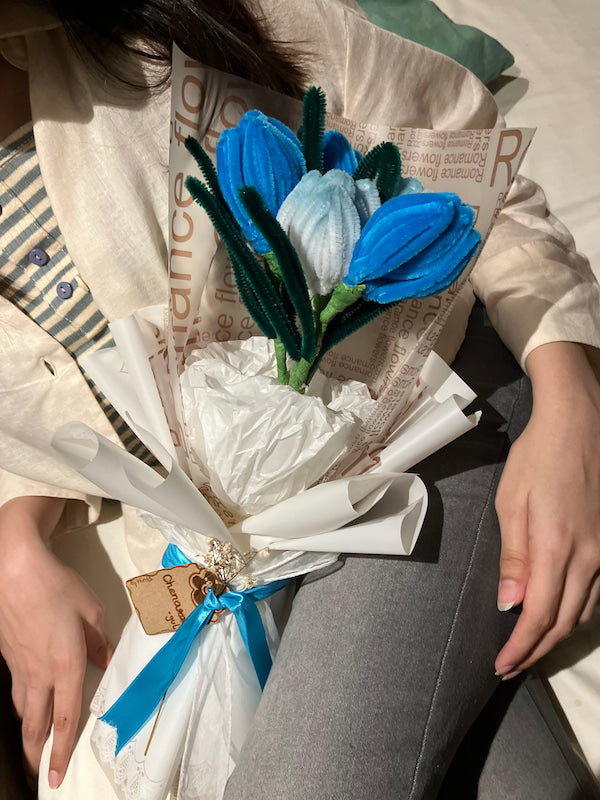 Bouquet of blue flowers wrapped in white paper with a blue ribbon on newspaper.